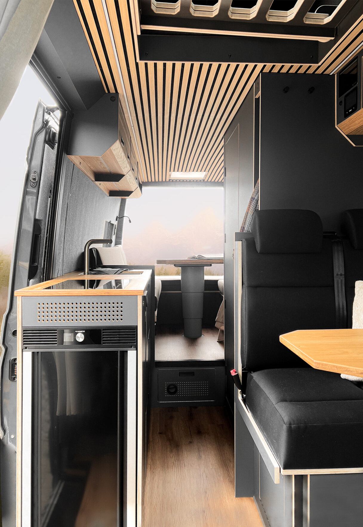 In schwarz gehaltener Ausbau eines Campers. Zu sehen ist ein großer Sitzbereich im Heck des Fahrzeuges und eine Küchenzeile in die eine Spüle, ein Herd und ein Backofen integriert sind.