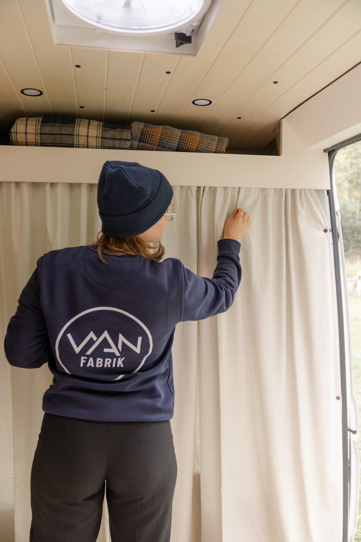 Eine Frau zieht den Vorhang in einem Van zu, der den Fahrerbereich vom Wohnbereich abtrennt