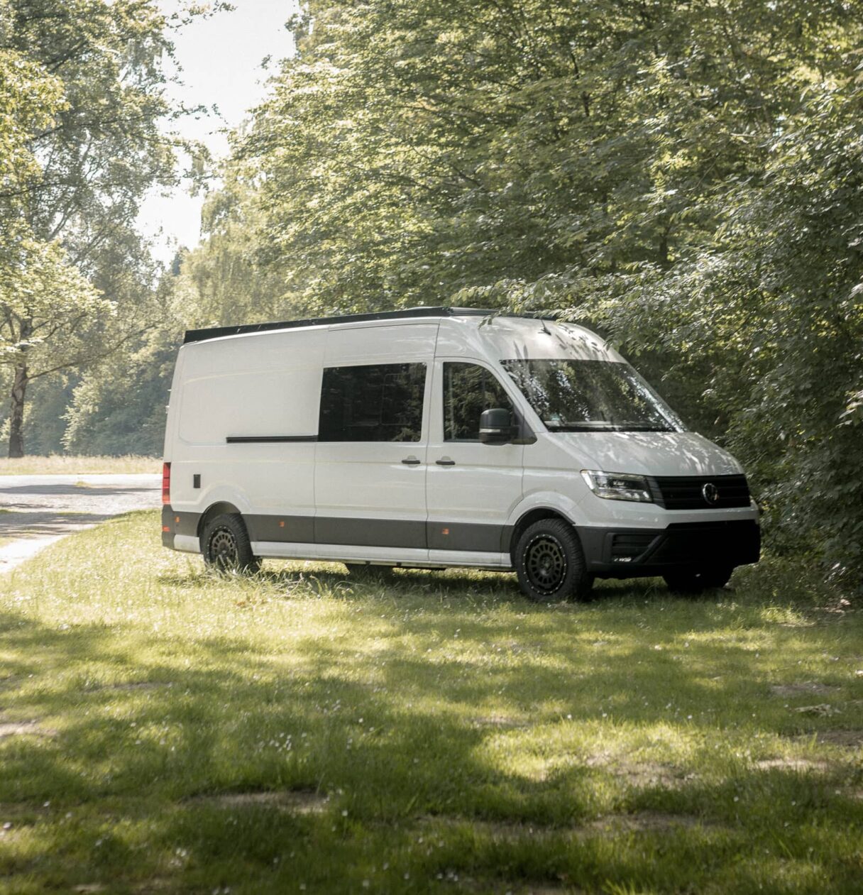 Seitenansicht eines VW Crafters der auf einer Wiese an einem Waldrand neben der Straße steht