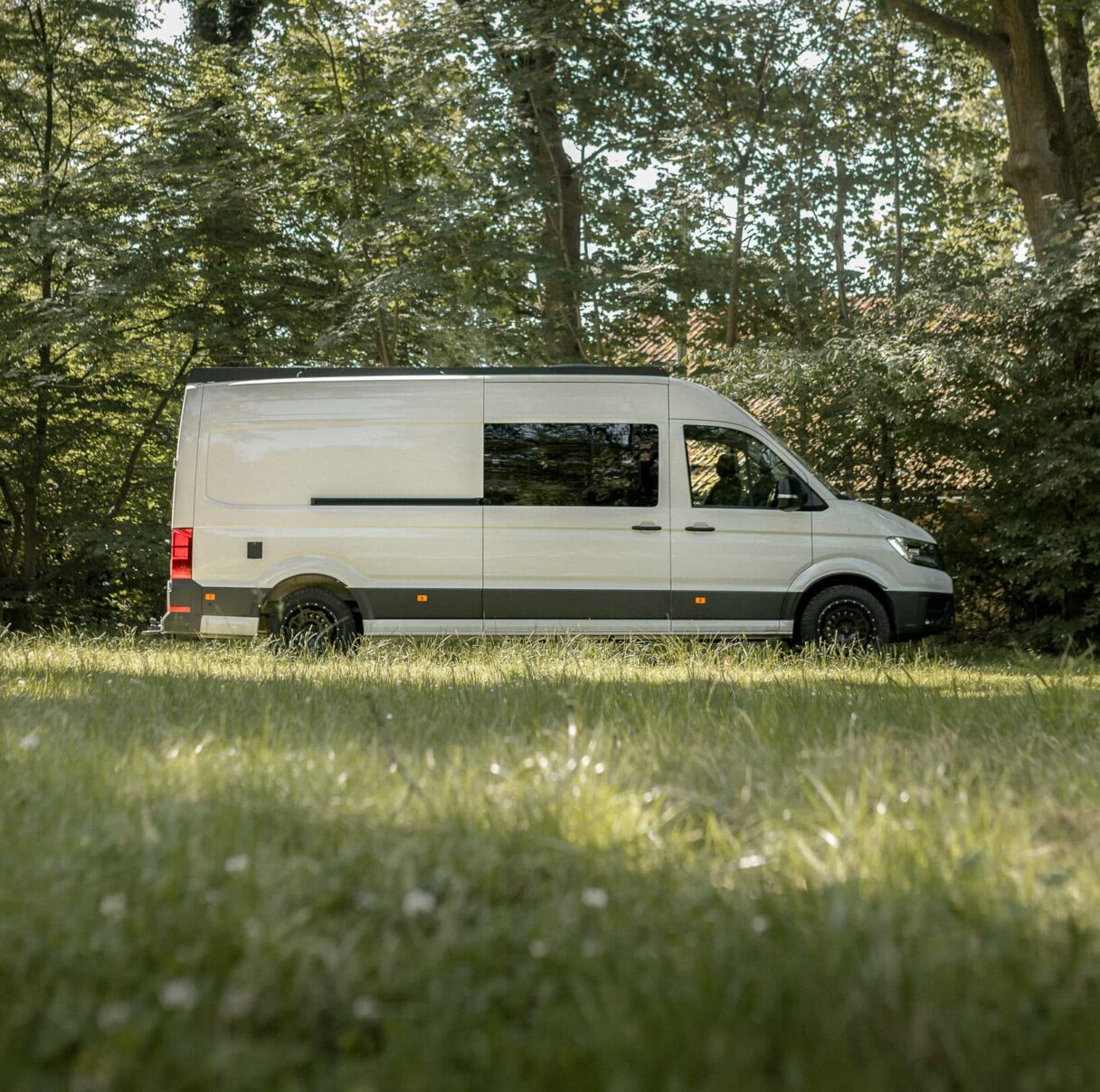 Seitenansicht eines weißen VW Crafter, der auf einer Wiese in einem Wald steht